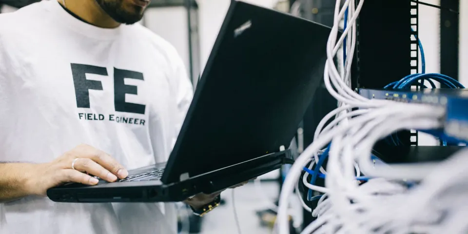 IT-Techniker prüft mit einem Laptop Netzwerkhardware bei der Bestandsaufnahme einer IT-Umgebung
