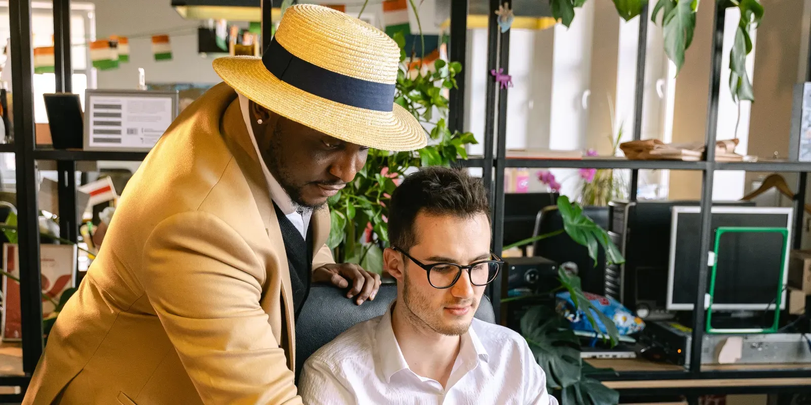 Ein Kollege unterstützt einen neuen Mitarbeiter an dessen Arbeitsplatz als Symbol für das IT-Onboarding neuer Mitarbeiter