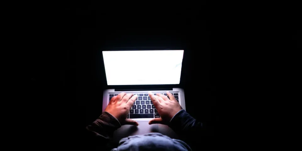 Person tippt in dunkler Umgebung auf einem Laptop