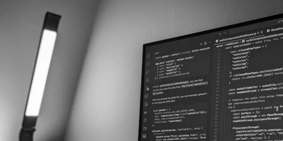 Ein Monitor mit Programmcode steht neben einer Schreibtischlampe.
