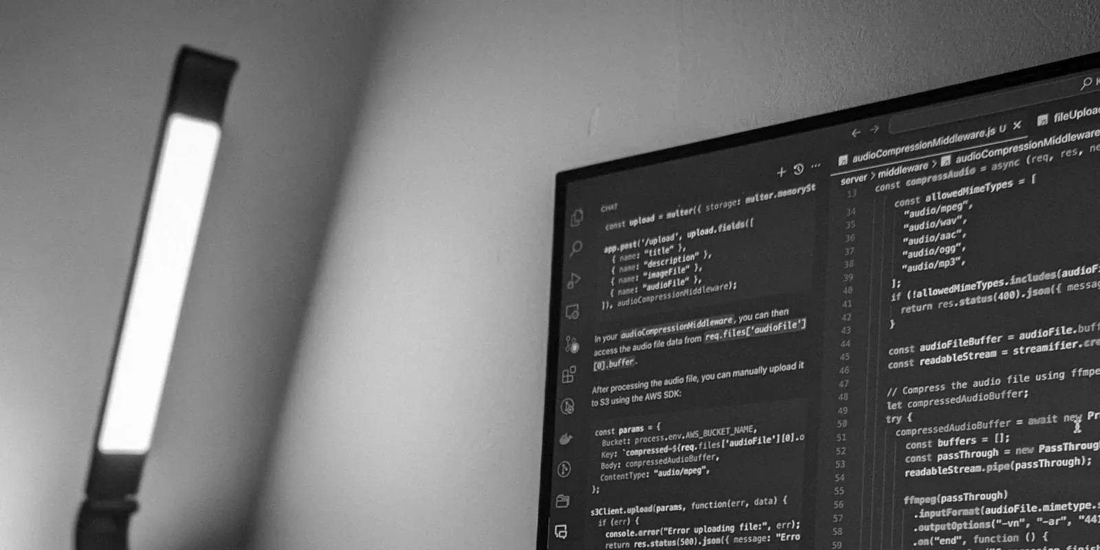 Ein Monitor mit Programmcode steht neben einer Schreibtischlampe.