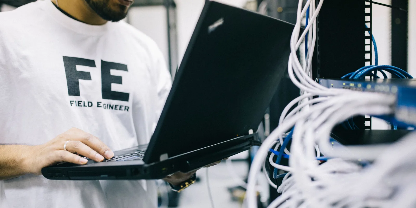 IT-Techniker prüft mit einem Laptop Netzwerkhardware bei der Bestandsaufnahme einer IT-Umgebung